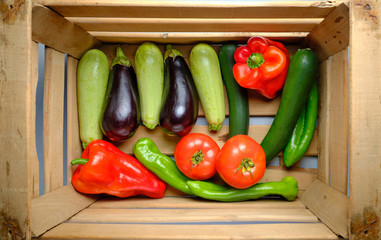 Old wooden box full of freshly harvested fresh vegetables, with red and green peppers, eggplants, zucchini and tomatoes