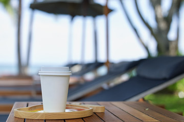 Fototapeta na wymiar Takeaway cup of coffee on table at beach hotel
