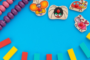 Frame from kids toys, top view on children's educational games on blue paper background. Multicolored wooden bricks, abacus, cute butterfly, ladybug, bee, spider. Flat lay, copy space for text