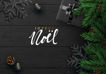 French text Joyeux Noel. Christmas background. Dark Wood plank texture, black snowflakes, realistic pine cone, decorative bauble, gift boxes. Xmas decoration objects. pine branches. Flat lay, top view