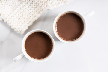 White ceramic cups of hot cocoa on top of white marble background, top view