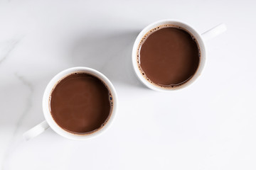 White ceramic cups of hot cocoa on top of white marble background, top view