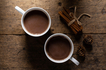White ceramic cups of hot cocoa on top of rustic wooden background, top view