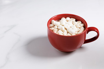 Red ceramic cups of hot cocoa with marshmallows on top of white marble background
