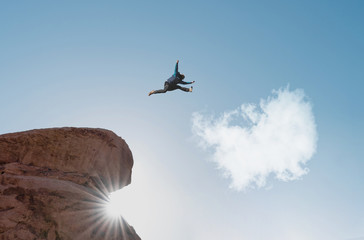 Silhouette a man jumping from cliff to white cloud. Challenge, risk, freedom and imagination concept