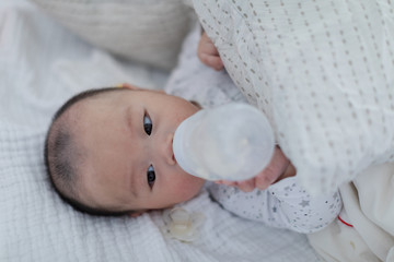 Baby drinking milk from bottle on bed, closeup