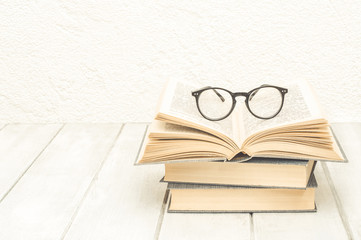 Stack of books with an open book and reading glasses on white wooden boards.  Education background