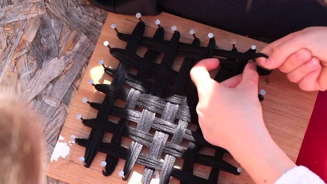 Leisure activity to create an eco-friendly tawashi sponge, with a homemade weaving loom from wood and nails. Red and black handcraft. Family, children activity. Shared team work, together. Happy day. 