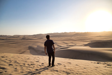 Fototapeta na wymiar young man on sand in a desert near Huacachina, Ica region, Peru. The sunset desert view