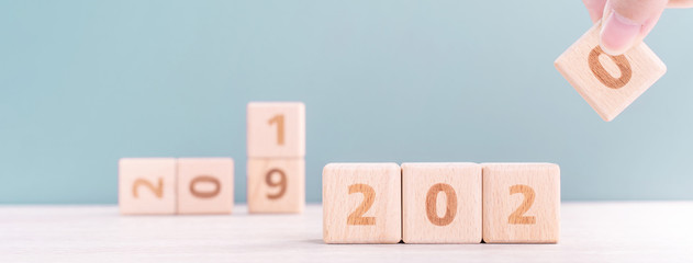 Abstract 2020 & 2019 New year countdown design concept - woman holding wood blocks cubes on wooden table and green background, close up, copy space.