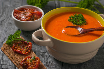 Cream of bell pepper soup with celery with dried tomatoes on a wooden table.
