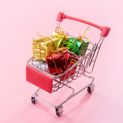 Annual sale, Christmas shopping season concept - mini red shop cart trolley full of gift box isolated on pale pink background, copy space, close up