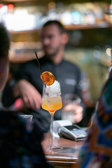 Yellow cocktail with orange slice and barman on the background
