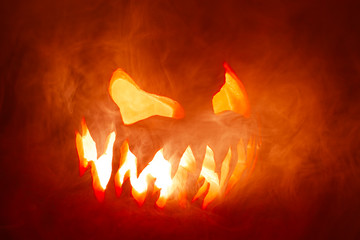Scary Halloween jack o lantern face glowing in smoke and fire.