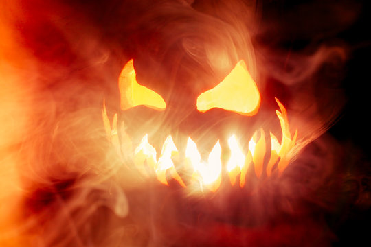 Scary Halloween jack o lantern face glowing in smoke and fire.