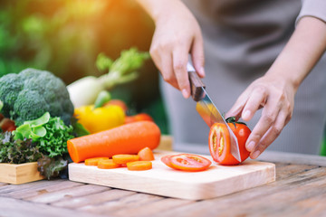 Closeup image of a woman cutting and chopping tomato by knife on wooden board