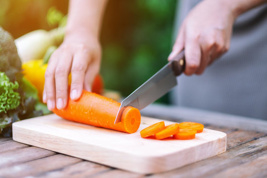Closeup image of a hand cutting and chopping carrot by knife on wooden board