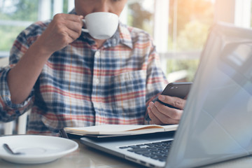 Man using smart phone and working on laptop computer in cafe