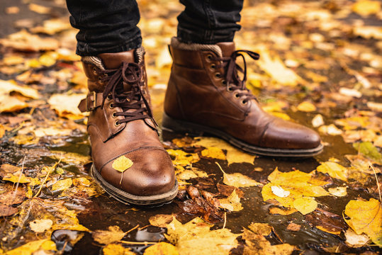 Male feet in leather boots standing in autumn puddle with colorful maple leaves all around. Fall season concept, autumn fashion