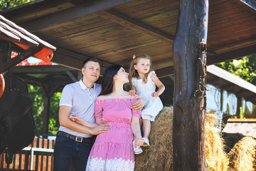 Beautiful happy family father, mother and cute little daughter together portrait on hay background on rural farm