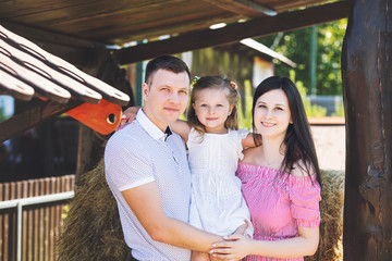 Beautiful happy family father, mother and cute little daughter together portrait on hay background on rural farm