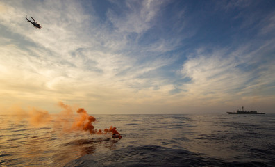 rescue ship and rescue helicopter searching for a man overboard in the sea with an orange smoke...