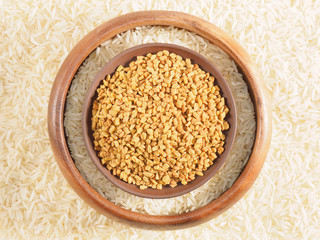 Rice in bowl and fenugreek in clay, plate. Background from basmati rice. Indian cuisine ingredients