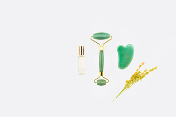 Gua sha stone, jade roller, and clear perfume bottle / still life arranged with golden wildflowers and isolated on white surface / natural holistic beauty concept