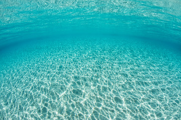 Bright sunlight ripples across a sandy seafloor in the tropical Pacific Ocean.