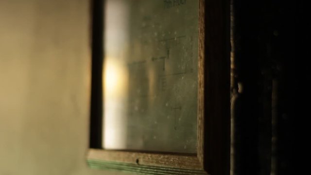 Slow-motion of reflections off of a framed picture in a shaded hallway