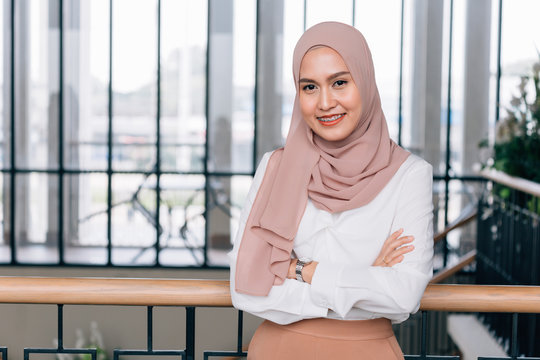 Young happy and successful South East Asian Islamic business woman with arms crossed in business corporate building setting looks at camera