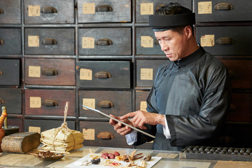 Traditional Chinese medicine practitioner following recipe on tablet computer when packing ingredients for customer