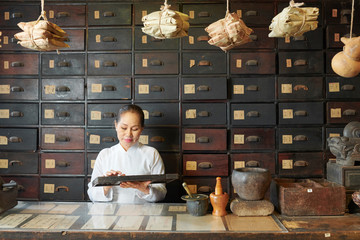 Traditional Chinese medicine practitioner using abacus for counting ingredients in her store