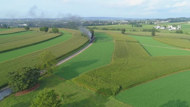 An Aerial View of a Steam Train Puffing Smoke Through Farm Countryside on a Sunny Summer Day with Green Fields