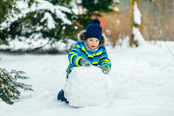 Fototapeta na wymiar little cute boy making snowman. rolling big snowball
