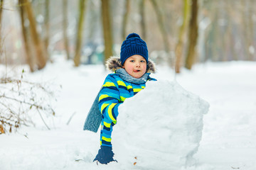 little cute boy making snowman. rolling big snowball