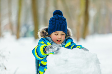 little cute boy making snowman. rolling big snowball