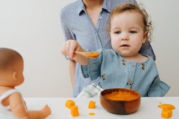 A girl holds out a spoonful of food, wants to feed the doll
