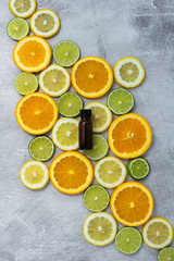 sliced oranges, lemons, and limes with essential oil bottles, amber bottles for aromatherapy oil, citrus rounds in lines on light background, copy space, copyspace