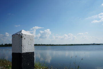 White-black concrete guide pillars with a blurred background of the reservoir and the sky.