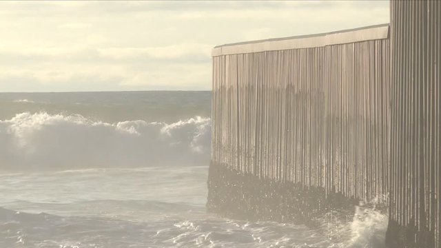 border barrier dividing Tijuana and San Diego oceans during golden hour