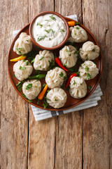 Spicy homemade khinkali with sour cream, pepper and herbs close-up on a plate. Vertical top view
