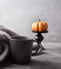 Obraz na płótnie Canvas Gray mug of coffee, pumpkin and gray scarf on the gray table. Autumn concept. Minimalism.