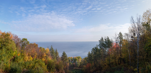 Fototapeta na wymiar Autumn forest on the hillsides on shore of reservoir