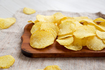 Salted wavy potato chips on a rustic wooden board on a white wooden background, side view. Close-up.