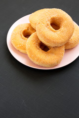 Homemade autumn apple-cinnamon donuts on a pink plate on a black background, low angle view. Copy space.