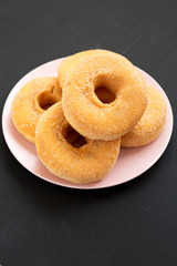 Homemade autumn apple-cinnamon donuts on a pink plate on a black surface, low angle view. Closeup.