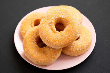 Homemade autumn apple-cinnamon donuts on a pink plate on a black background, side view. Close-up.