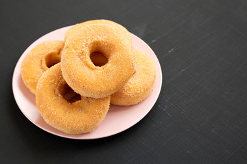 Homemade autumn apple-cinnamon donuts on a pink plate on a black background, side view. Space for text.