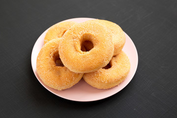 Homemade autumn apple-cinnamon donuts on a pink plate on a black surface, side view. Closeup.